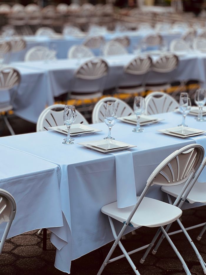 gallery-04 Rows of white tables set for an outdoor event with elegant arrangements.
